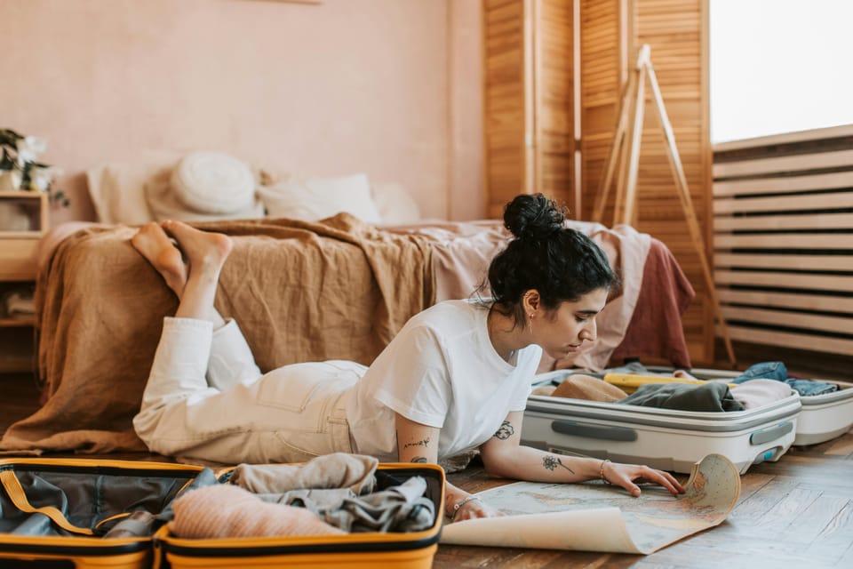 Young woman packing a suitcase and reading maps in her bedroom, preparing for an exciting travel adventure.